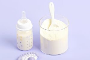 biberon-lait-infantile-poudre-cuillere Biberon rempli de lait infantile à côté d’un récipient de poudre avec une cuillère doseuse