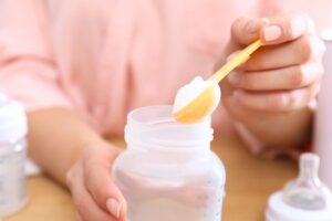 preparation-lait-infantile-poudre-biberon Parent versant du lait infantile en poudre dans un biberon