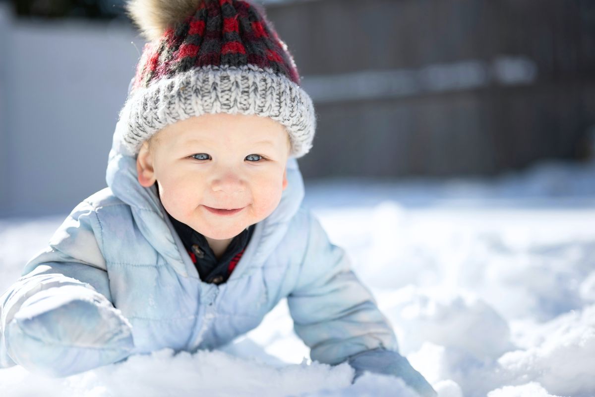 Bébé souriant habillé chaudement en combinaison d'hiver et bonnet, jouant dans la neige