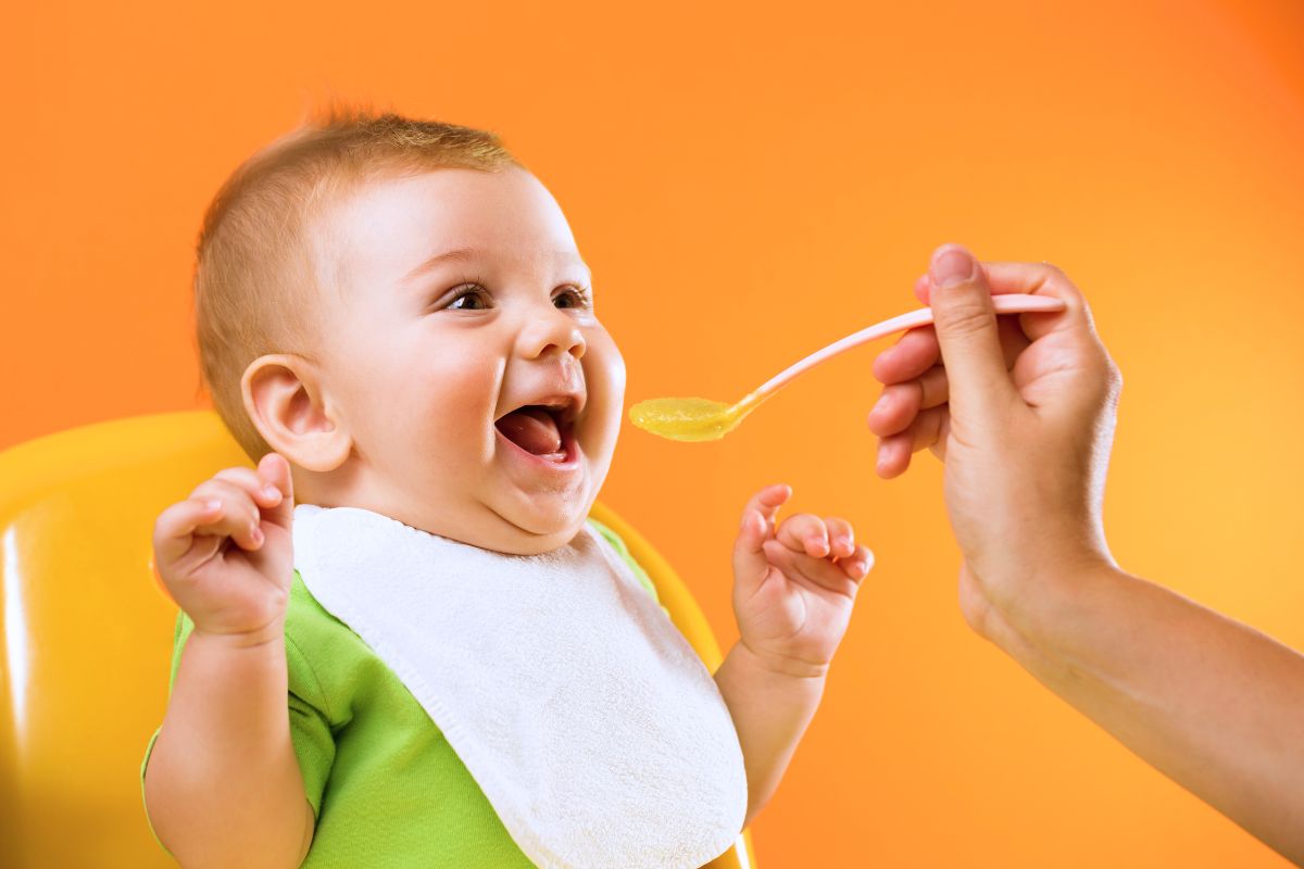 Bébé souriant pendant qu'on lui donne de la purée à la cuillère