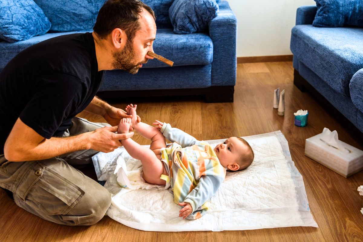 Papa changeant la couche de son bébé sur le sol à la maison avec des lingettes et des couches