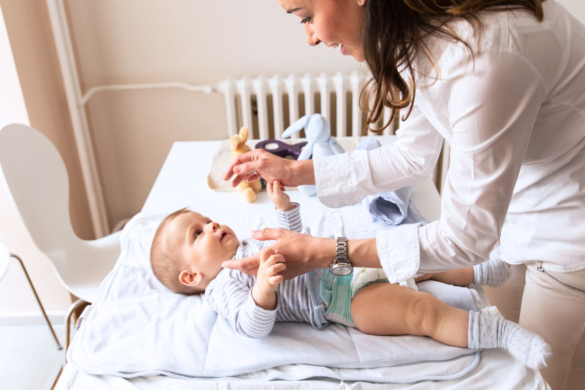 Maman souriante change la couche de son bébé sur une table